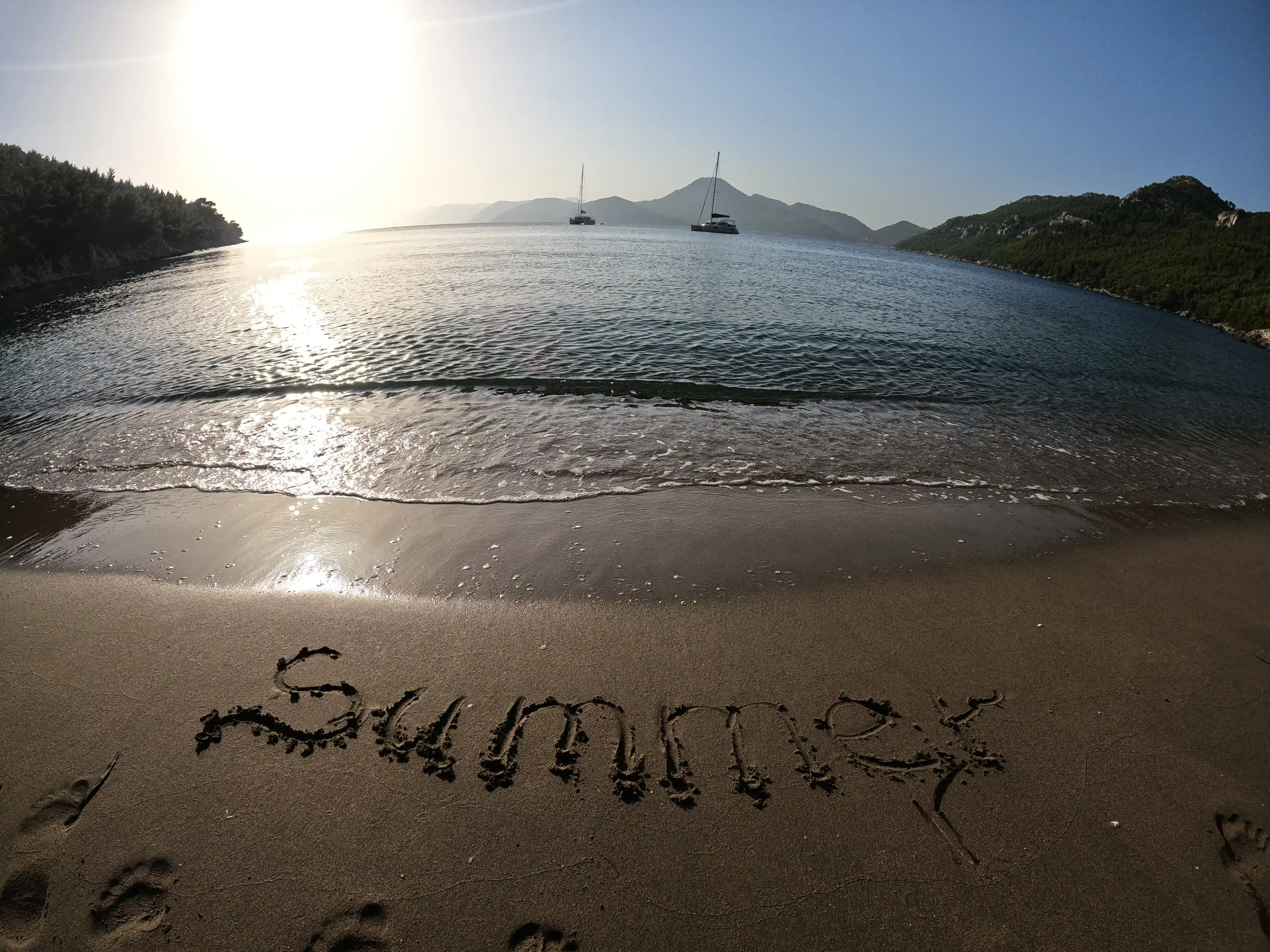 Sandy beach and the horizon view with two catamarans and islands, Summer written in the sandy beach